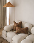 Beige sofa with brown textured pillows in a room with a standing lamp and curtains