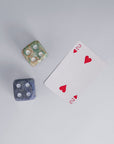 A pair of two hand-carved gemstone dice, in blue and multi-color, displayed on a white surface next to the two of hearts playing card.