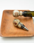 Two decorative bottle stoppers on a wooden tray with a white background