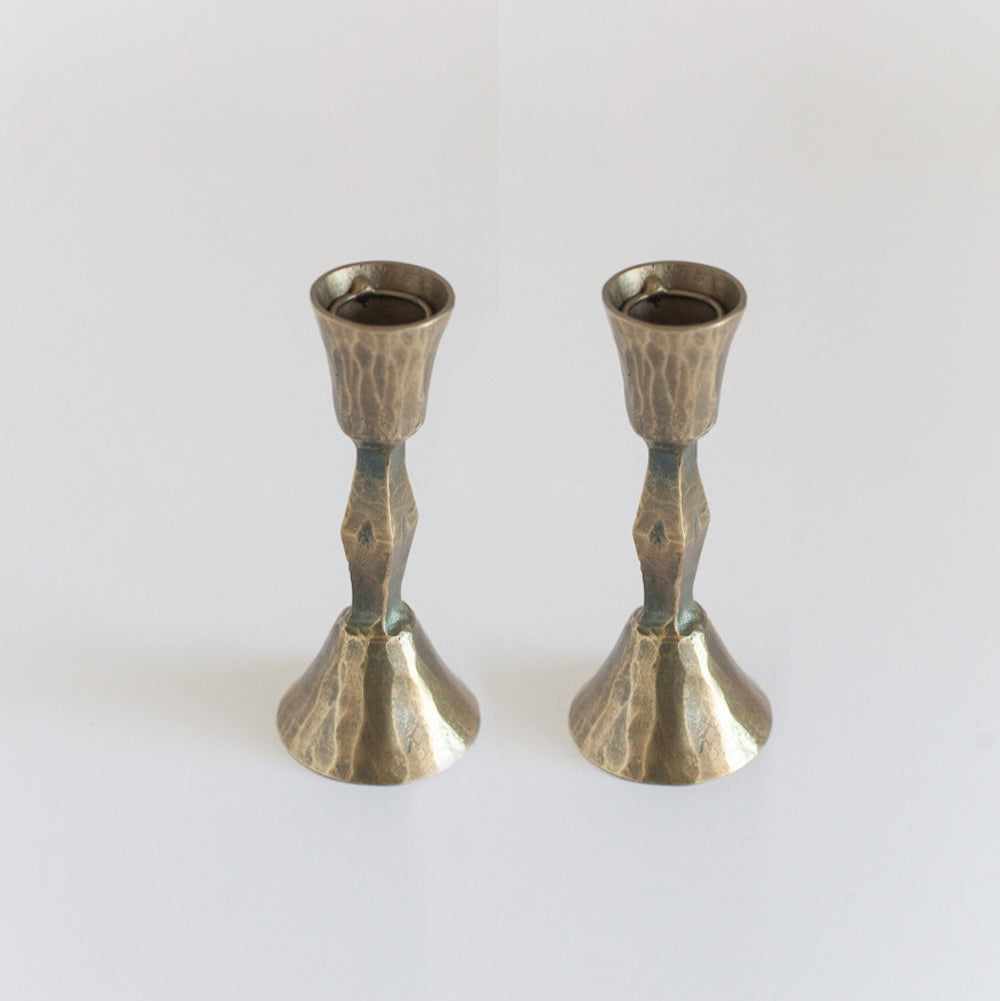 A pair of hand-forged iron candle holders with a brass finish, featuring a textured design.