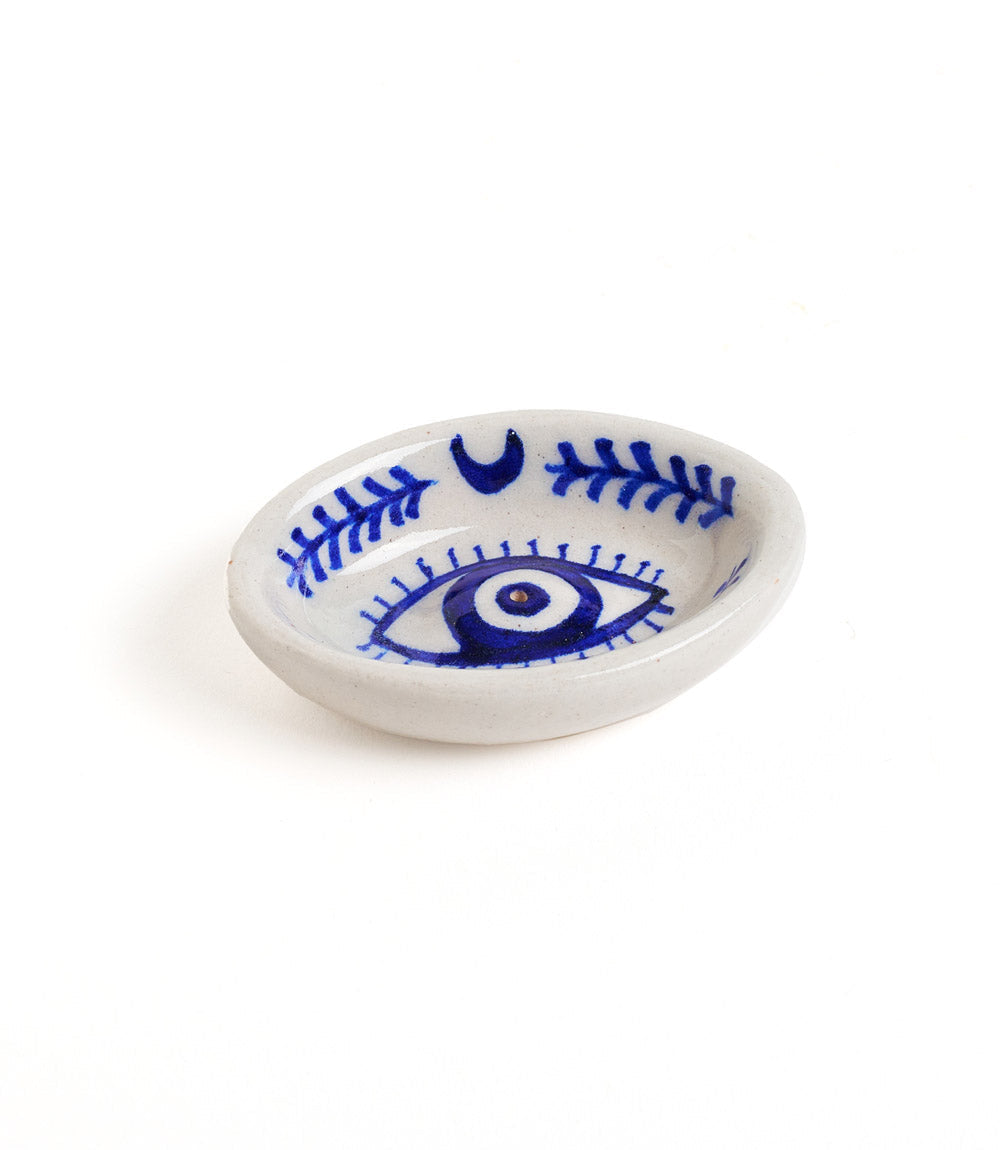 A hand painted blue and white ceramic incense holder with a geometric pattern and an evil eye motif in the center