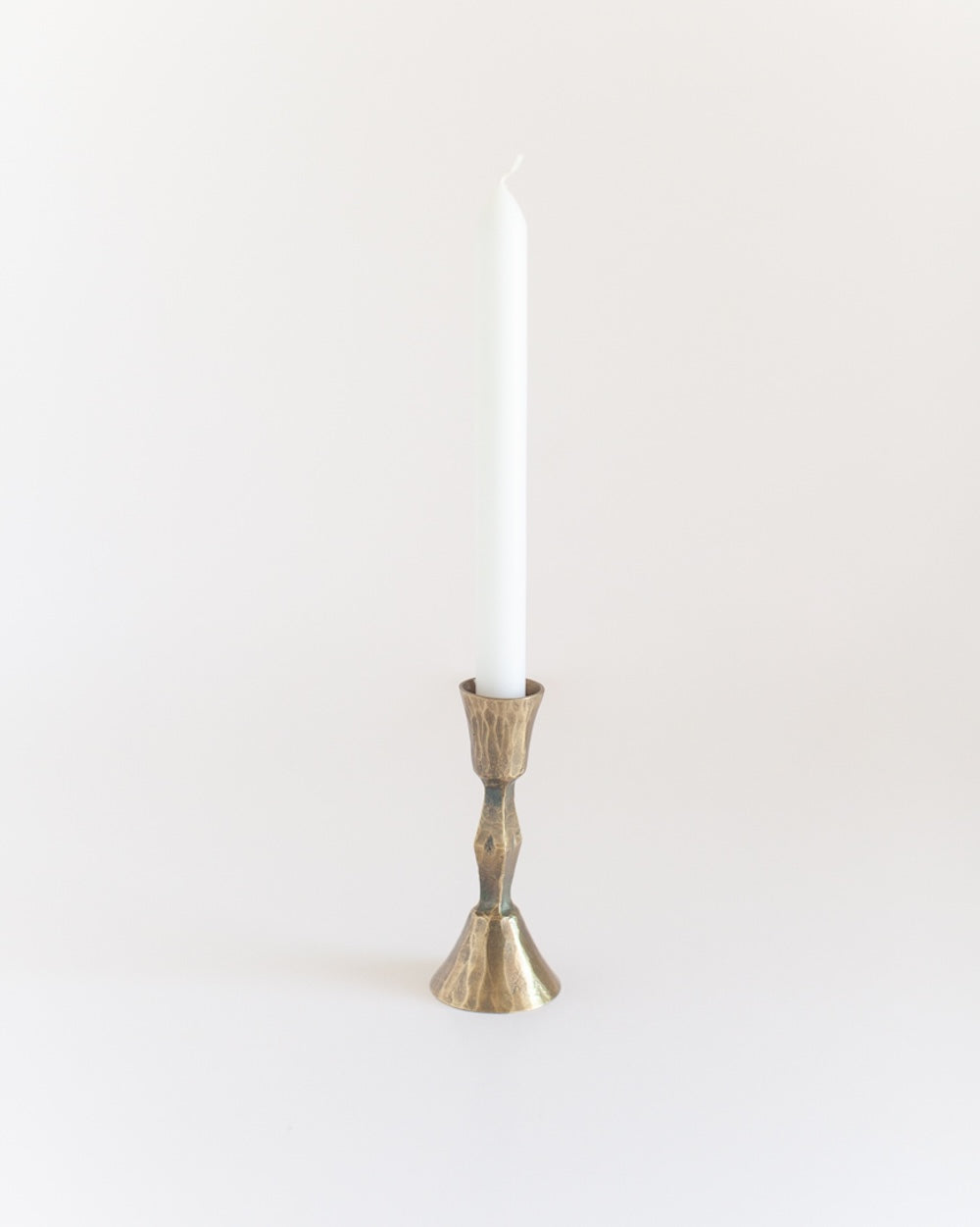 Bronze candle holder with a white candle on a light beige background