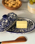A hand-crafted ceramic blue and white butter dish with butter inside next to a butter knife