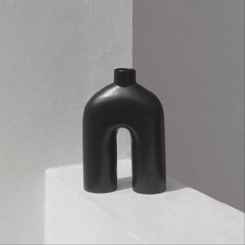 A black, handmade ceramic vase with an abstract shape, featuring a wide base that narrows at the neck, displayed against a neutral background.