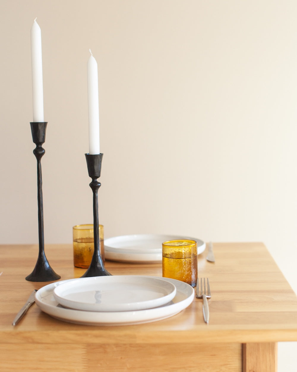 Dining table set with plates, glasses, and candles against a plain wall.