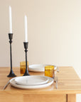 Dining table set with plates, glasses, and candles against a plain wall.