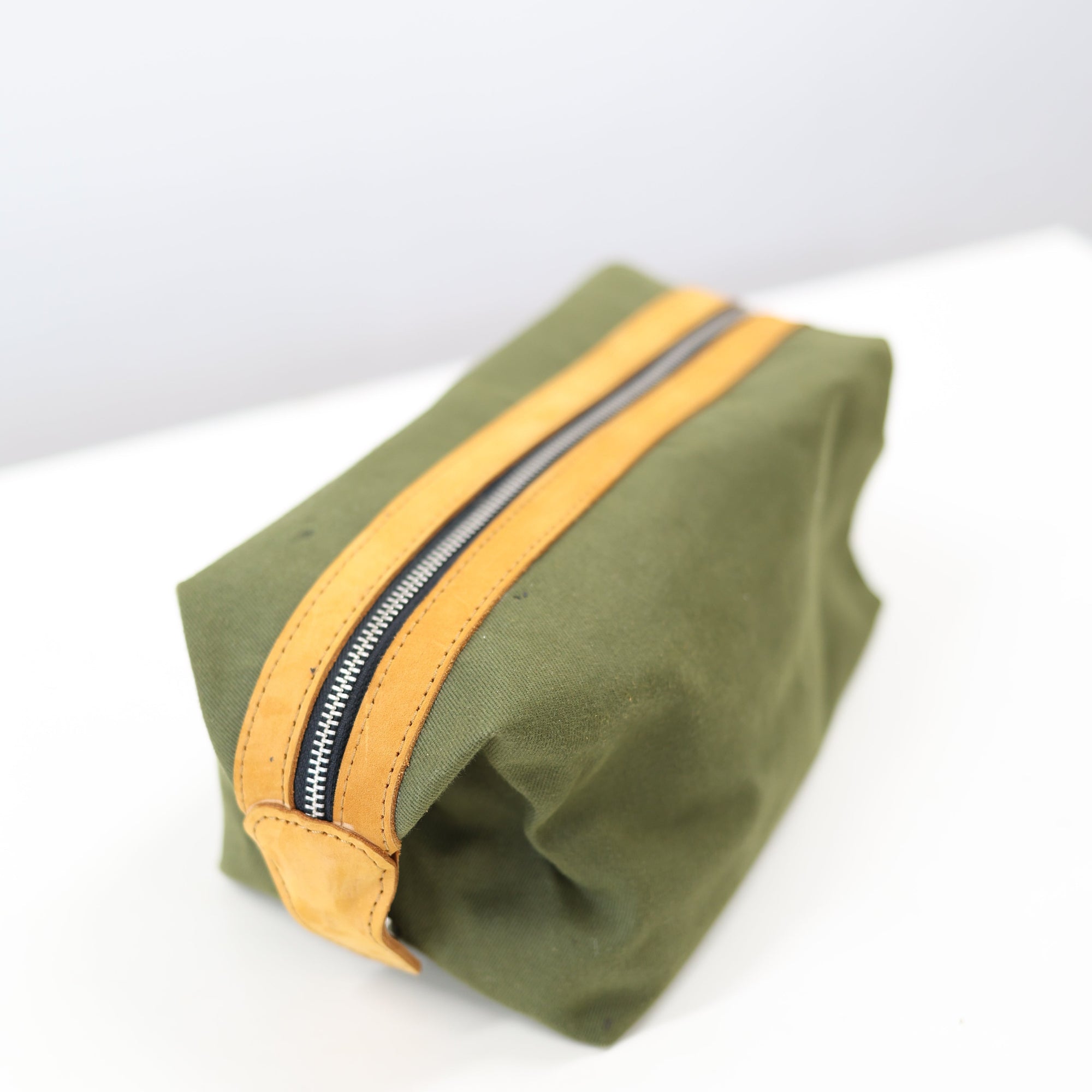A green toiletry bag with leather accents and a metal zipper.