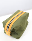 A green toiletry bag with leather accents and a metal zipper.