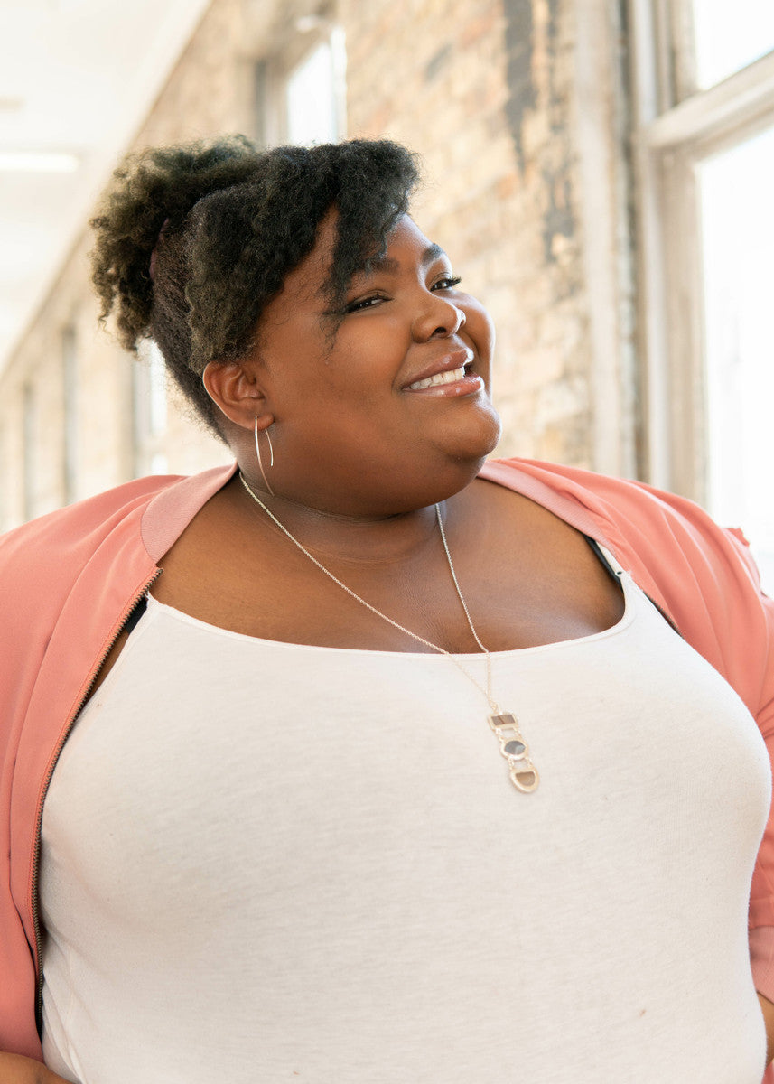 A model wearing a pair of brass recycled metal earrings and a necklace.