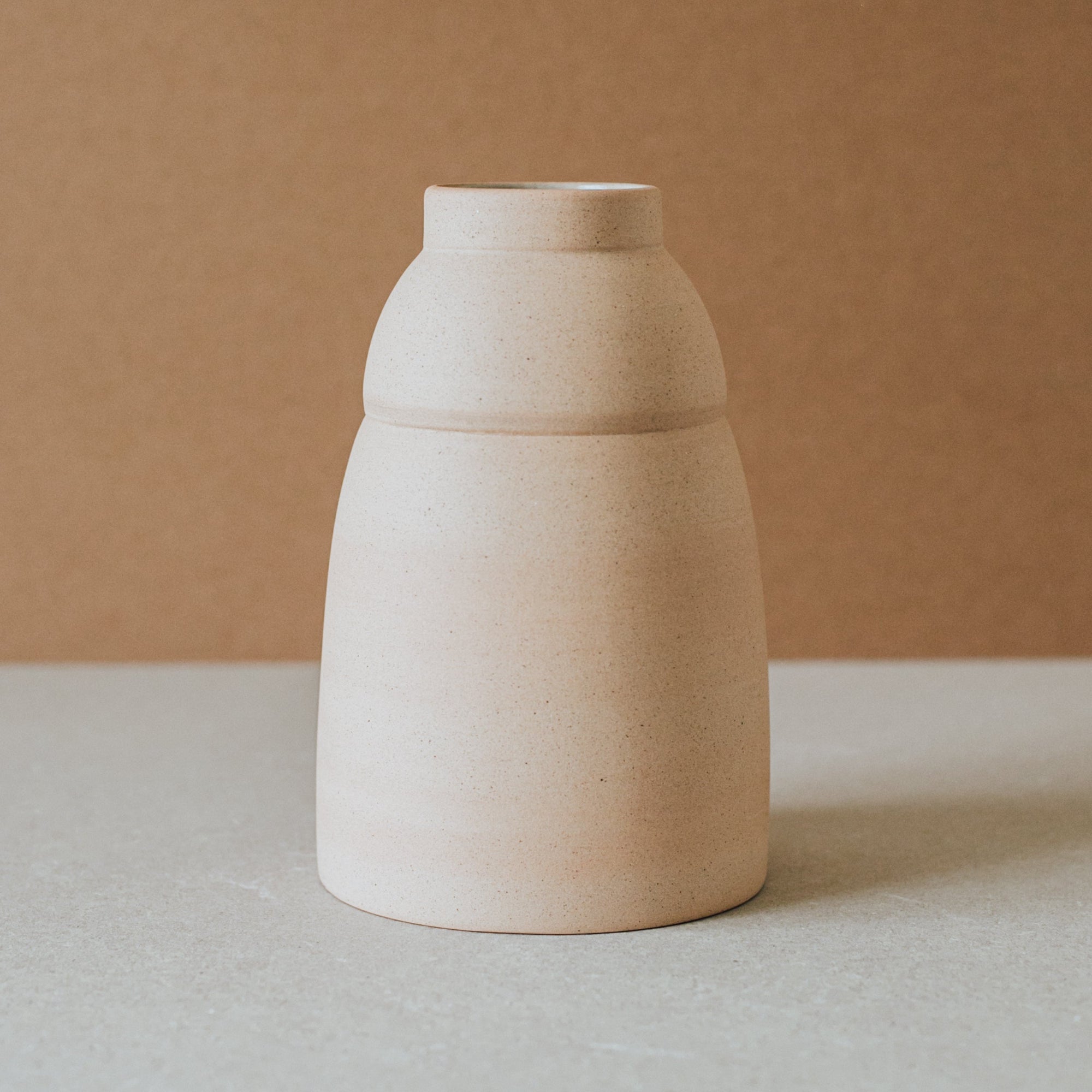 A beige ceramic vase with a rounded body and a narrower top, placed against a neutral background.