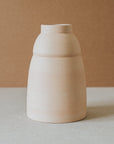 A beige ceramic vase with a rounded body and a narrower top, placed against a neutral background.