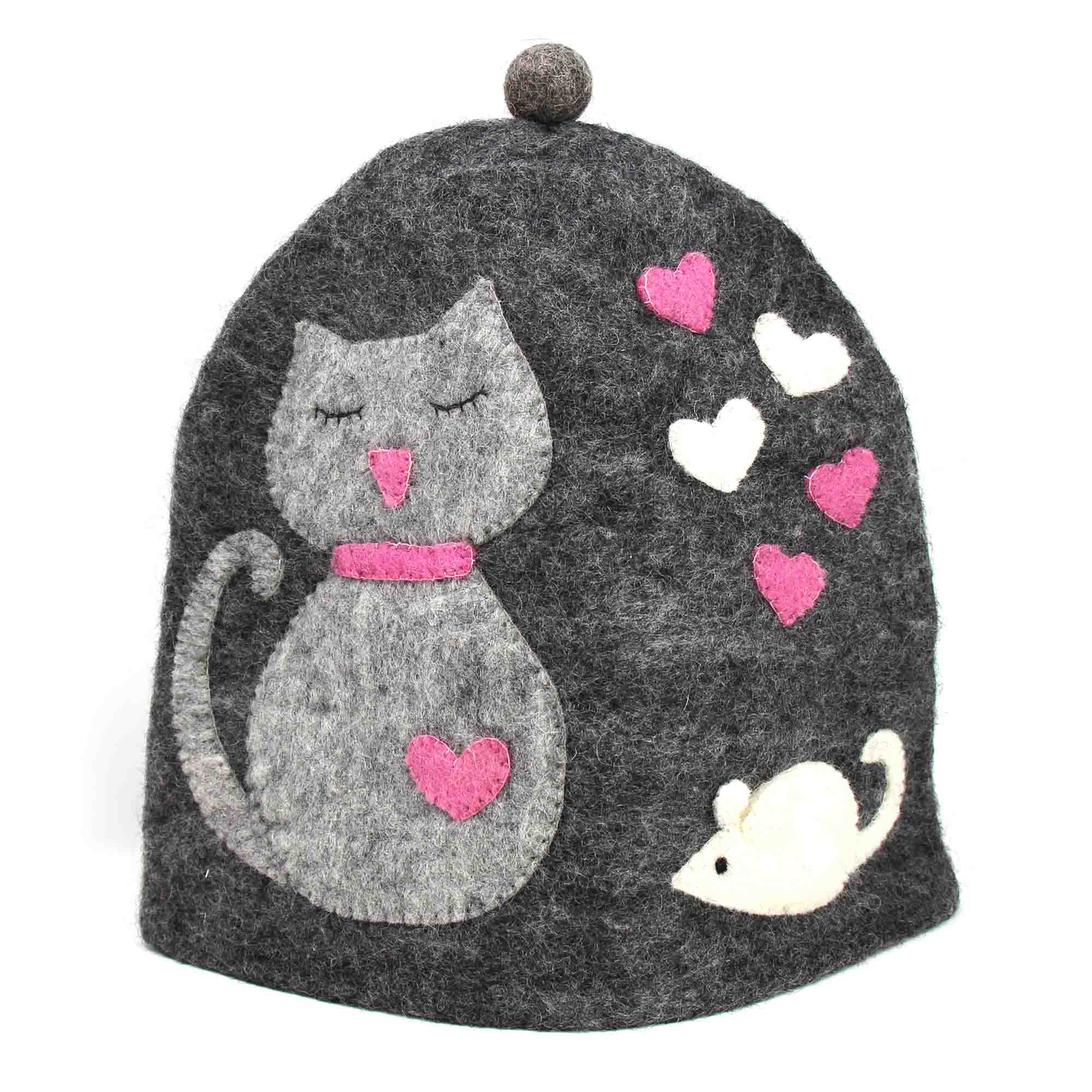 A gray felt tea cozy with a design of a sleeping cat, hearts, and a mouse