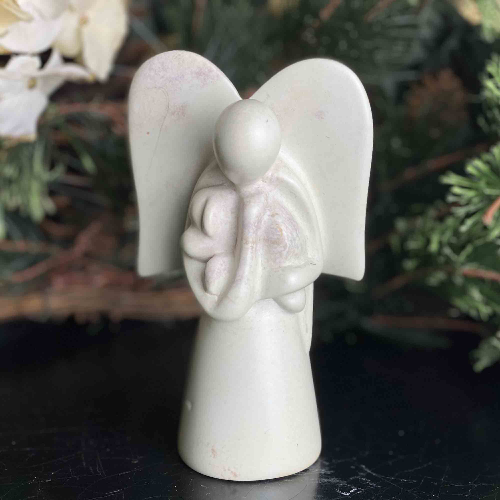 A hand-carved soapstone sculpture of an angel holding a dog in front of a christmas tree