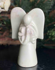 A hand-carved soapstone sculpture of an angel holding a dog in front of a christmas tree