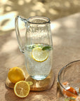 A clear glass pitcher with a hammered texture on a wooden table with a lemon inside