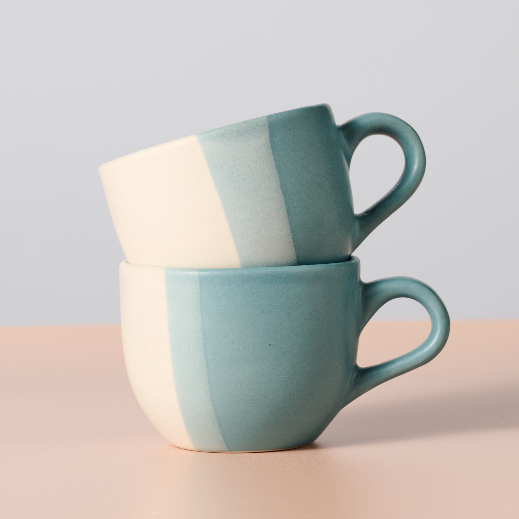 Two ceramic mugs with a two-tone design stacked on a light background