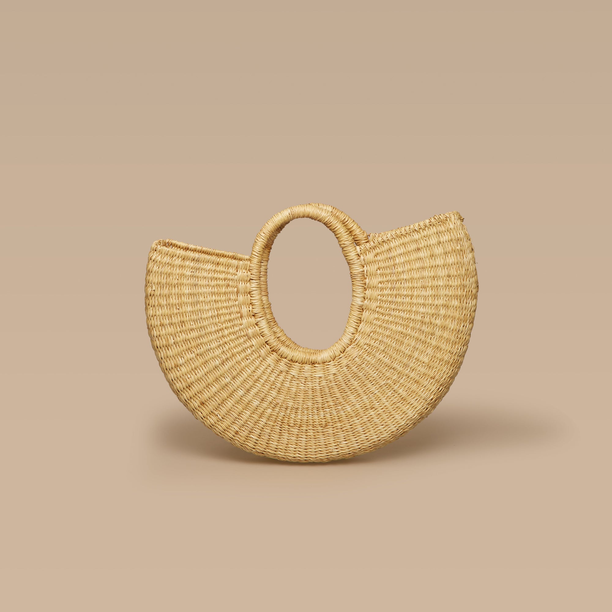 A beige half-moon shaped handbag made from elephant grass, with an open top and two handles.