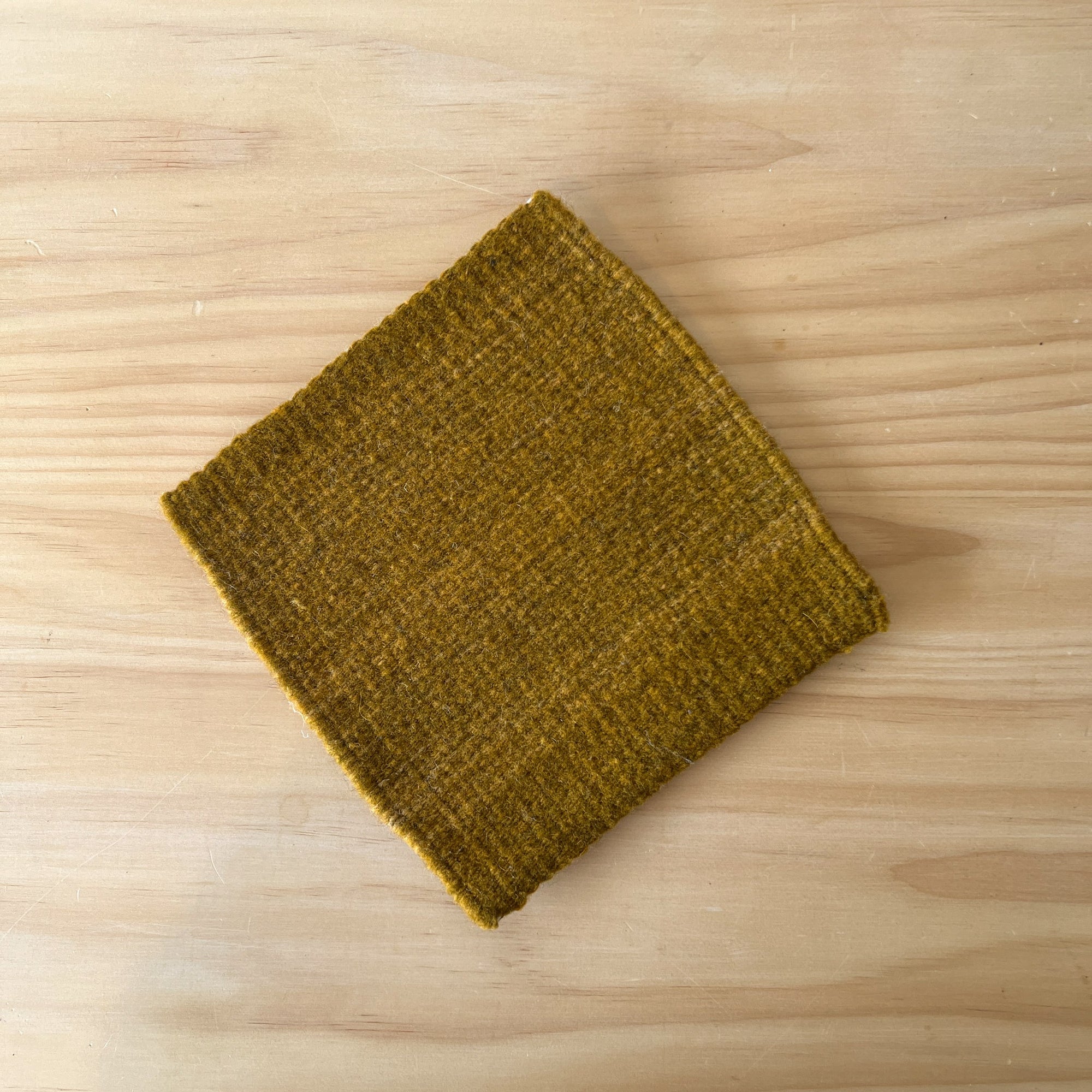 Folded green fabric square trivet on a wooden surface