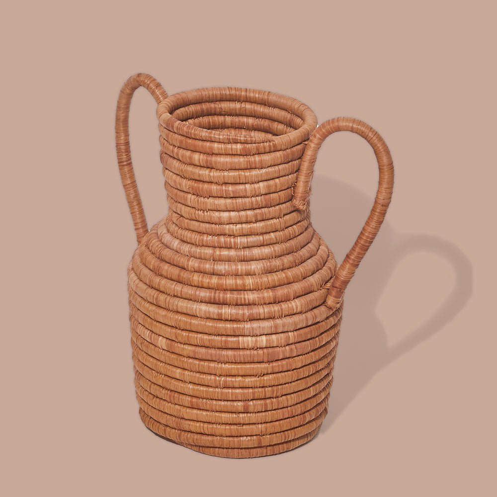 A beige, handcrafted vase with double handles made from strands of sisal wrapped around bunches of sweetgrass, displayed against a neutral background.