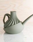 Green ceramic watering can with a textured design on a light wooden surface