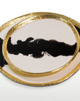 Two decorative plates with gold rims and black abstract designs on a white background