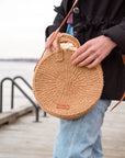 Person holding a round woven bag by a waterfront