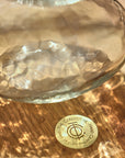 Glass bowl with a textured surface on a wooden surface, featuring a gold coin with text and symbols.