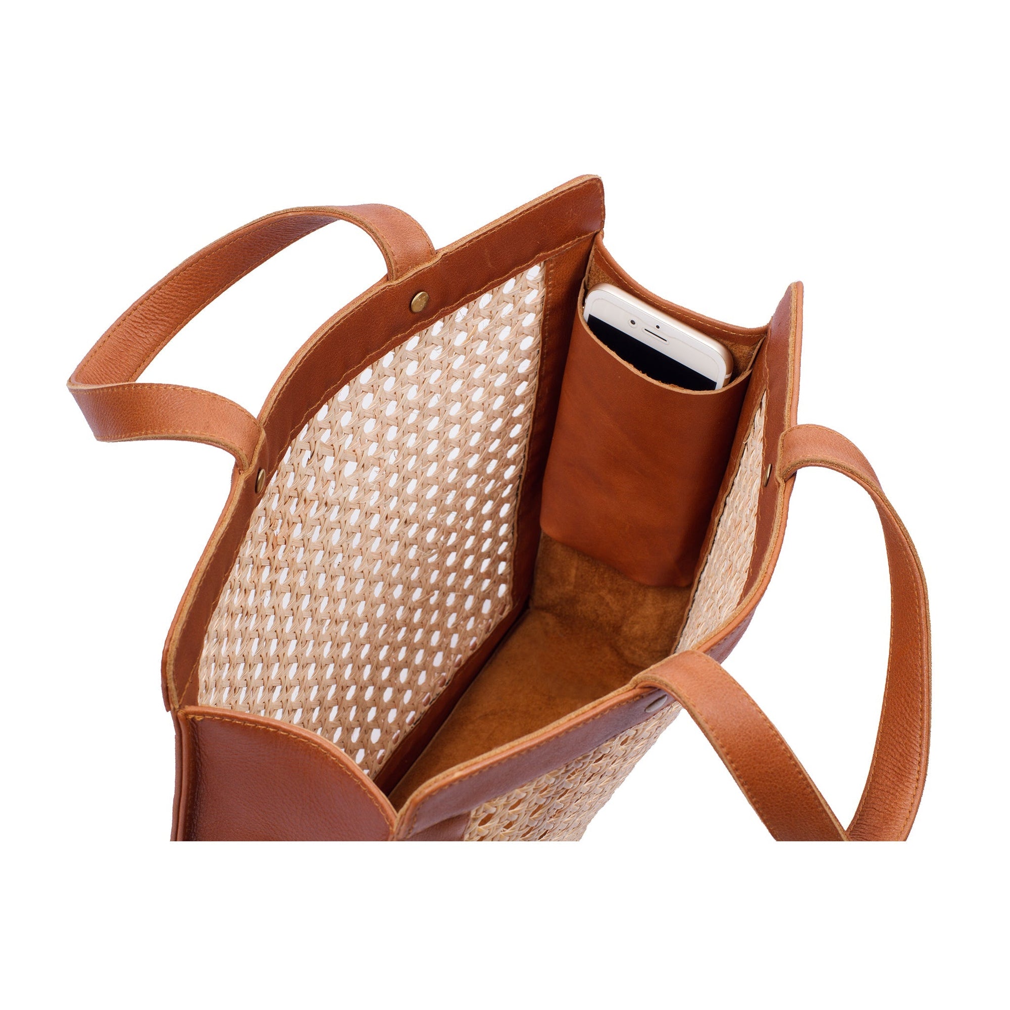 The inside of a brown leather tote bag with rattan cane webbing and leather handles with a phone in the side pocket.