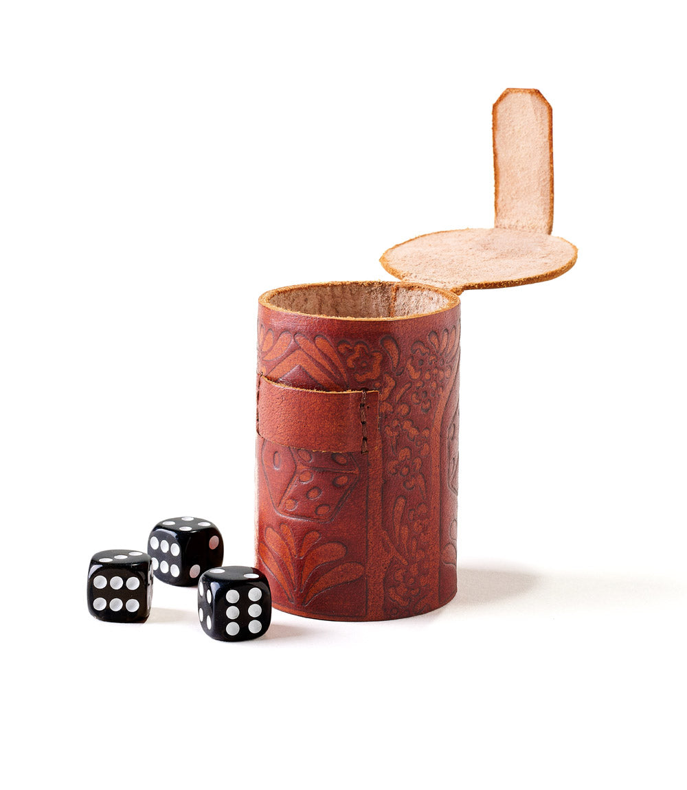 A hand tooled brown leather dice cup with a set of black and white dice in front of it.