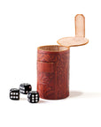 A hand tooled brown leather dice cup with a set of black and white dice in front of it.