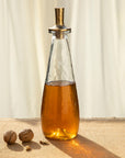 Glass decanter with a metal cap containing a amber liquid on a textured surface.