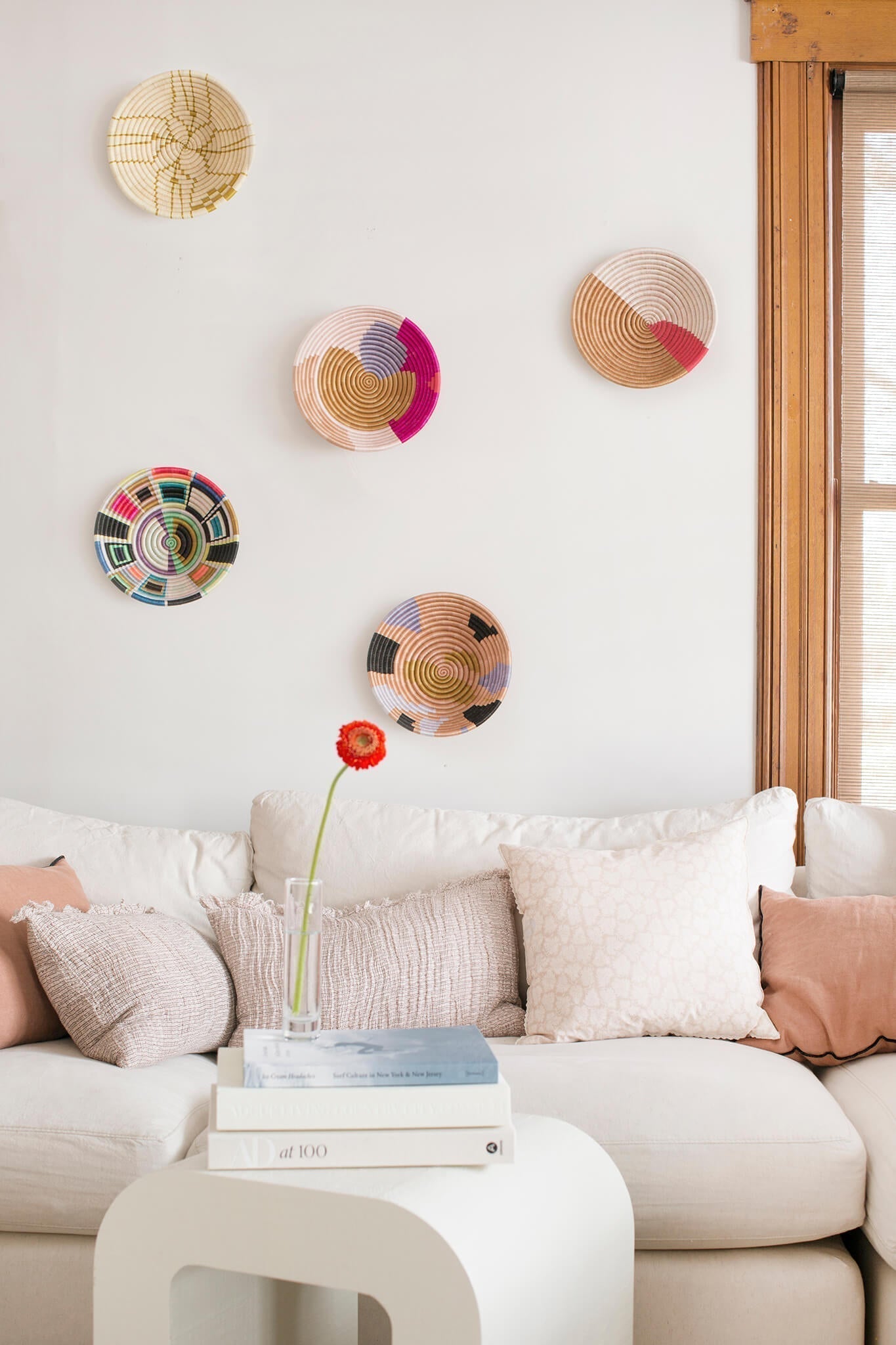 Five handwoven baskets with multi-color patterns hanging on a white wall behind a couch