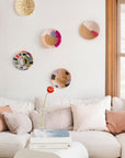 Five handwoven baskets with multi-color patterns hanging on a white wall behind a couch