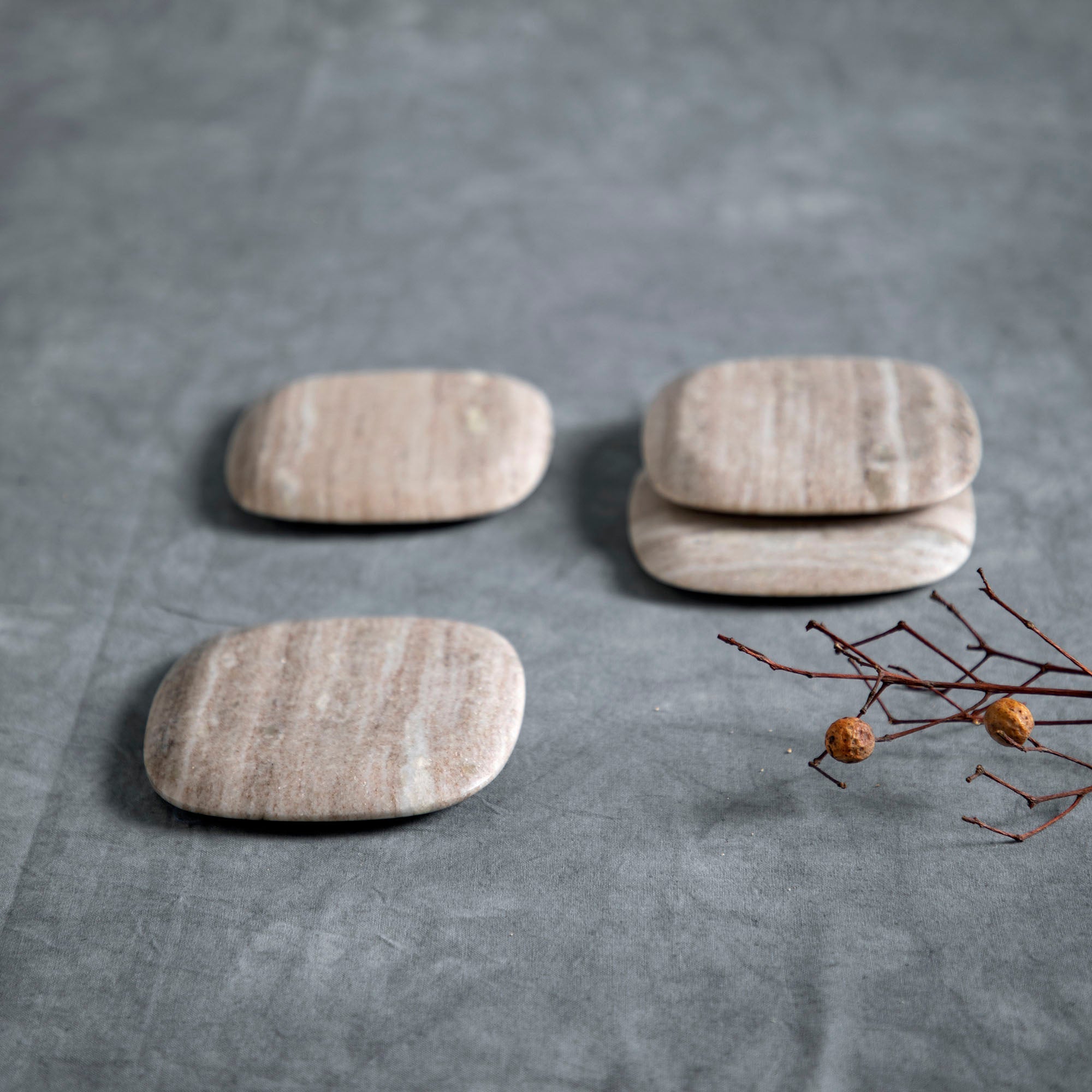 Three beige marble coasters on a gray surface with a branch and berries