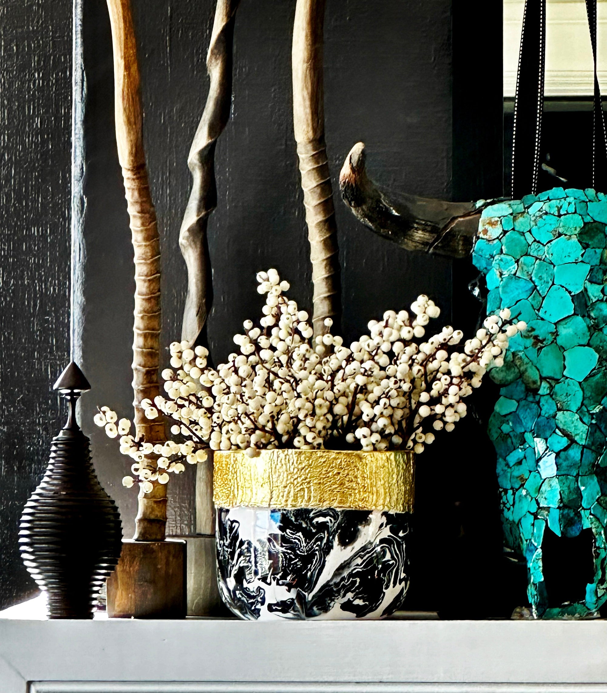 Decorative setup with a black and gold vase, white flowers, and a turquoise mosaic elephant against a dark background.