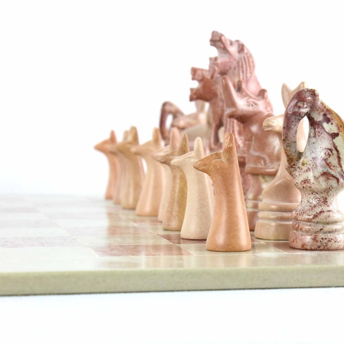 A hand-carved soapstone chess set with a green and pink checkered board and beige, pink, and white stone pieces zoomed in on the white pieces zoomed in on the pink pieces.