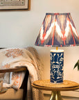 Decorative lamp with colorful shade on a table next to a chair with floral cushions and a plant.