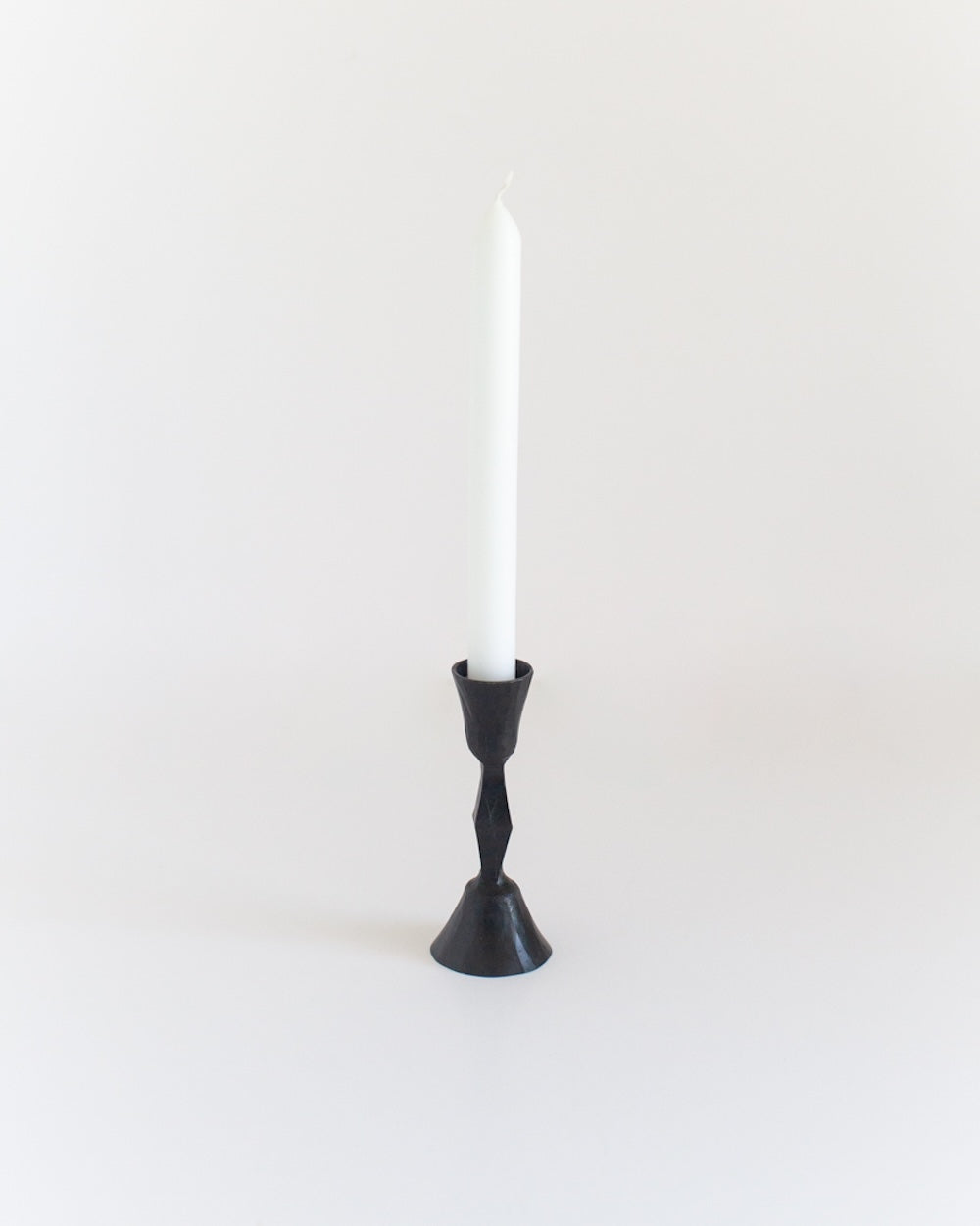 Black candle holder with a white candle on a light gray background