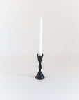 Black candle holder with a white candle on a light gray background