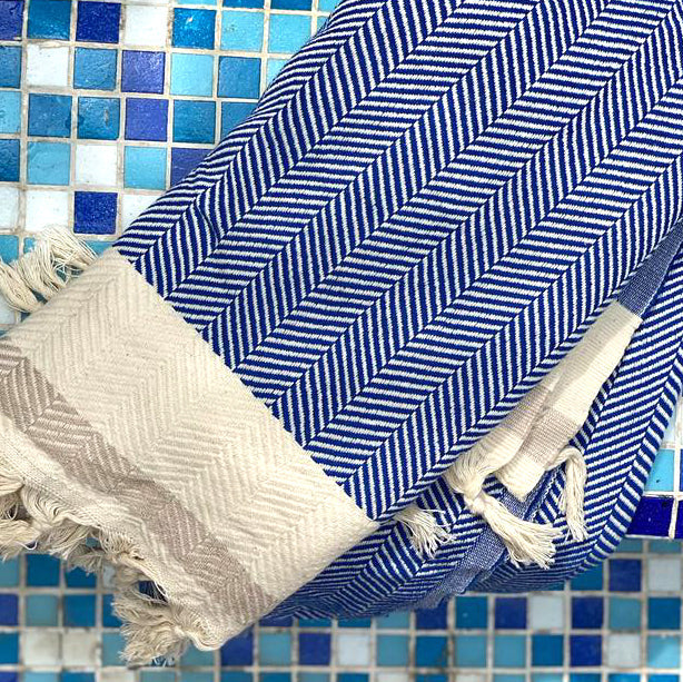 A blue and beige geometric patterned throw blanket with tassels on a tiled background
