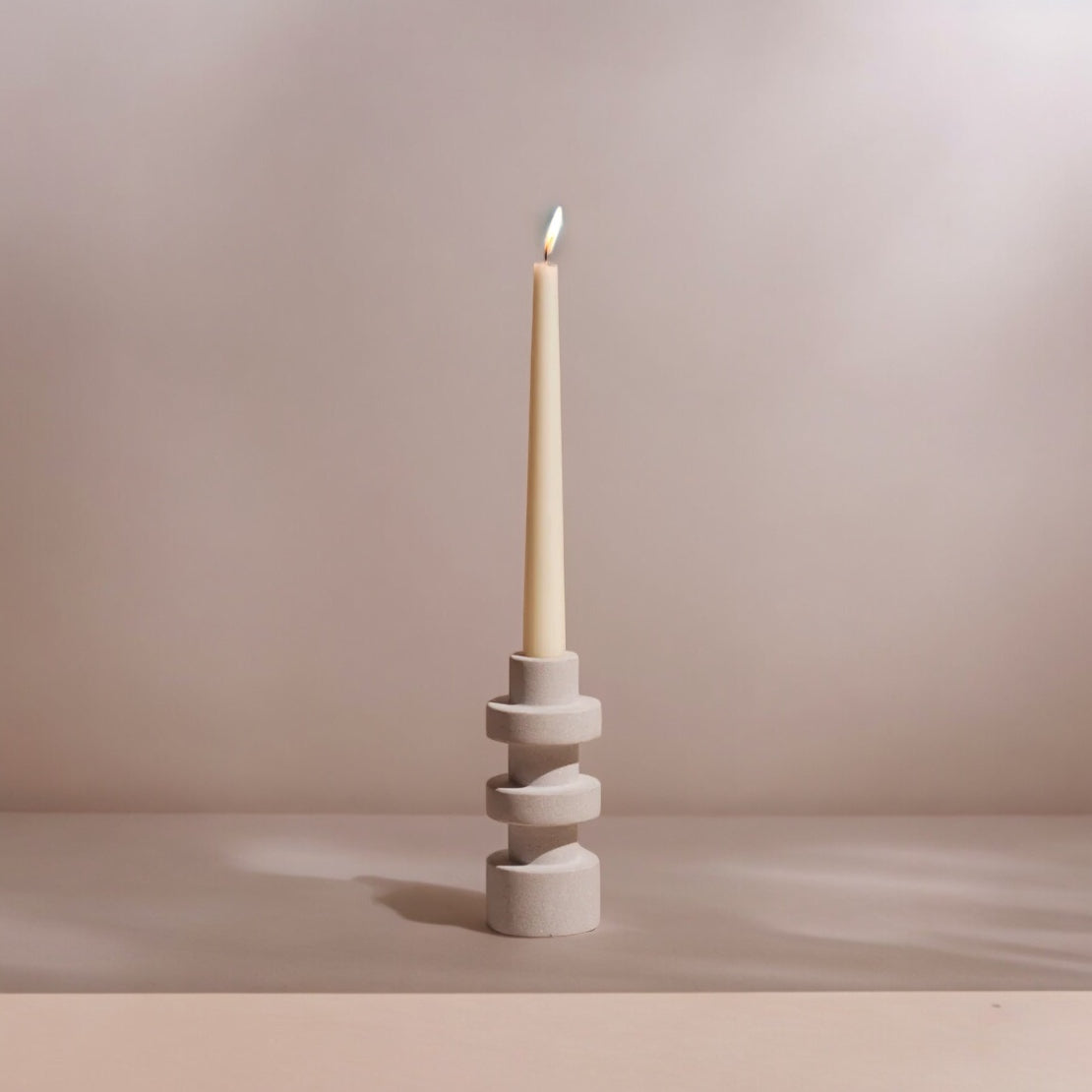 A natural sandstone taper candle holder with a candle lit on top, presented against a neutral background.