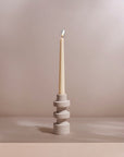 A natural sandstone taper candle holder with a candle lit on top, presented against a neutral background.