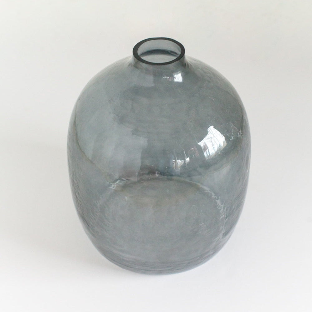 A blue grey hammered glass vase with a round shape on a white background.