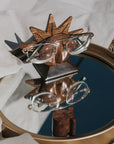 A wooden glasses holder with a sun face design, holding a pair of eyeglasses on a glass tray