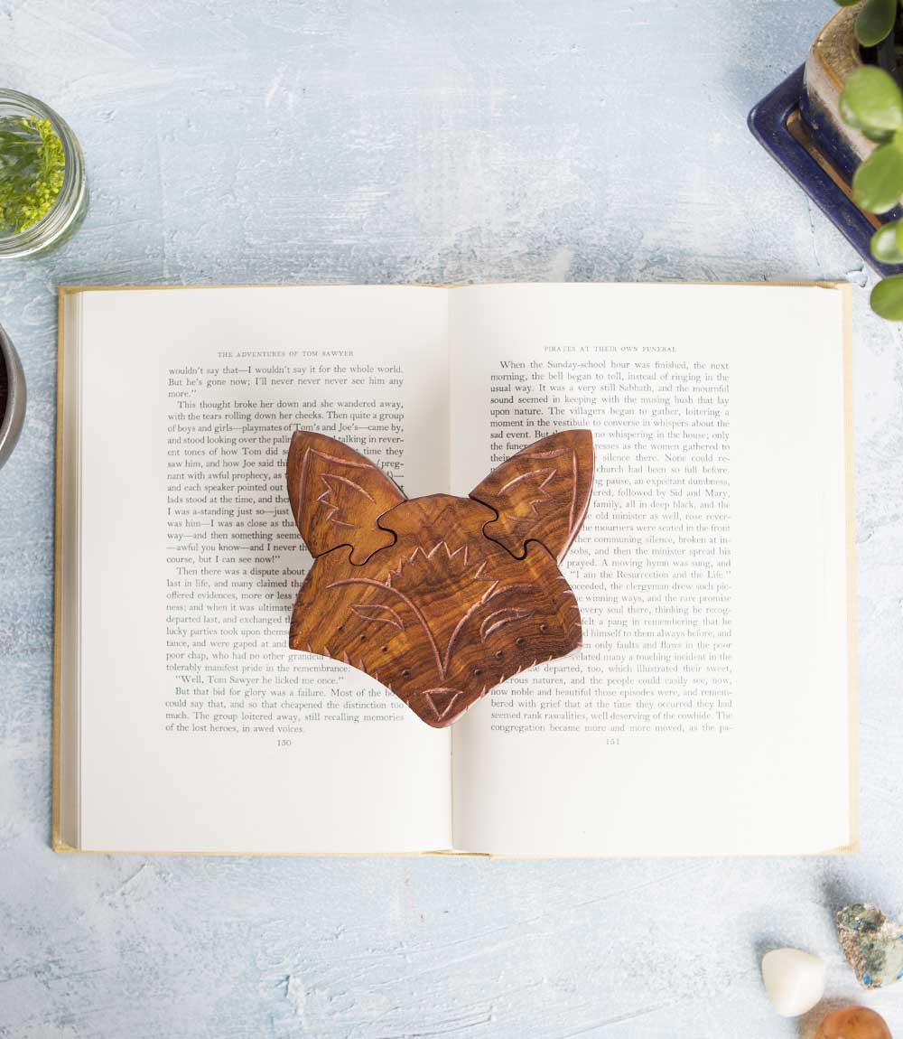 Hand-carved wooden fox face puzzle box with multiple pull-apart pieces on top of a book.