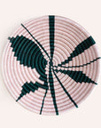 Round woven basket with pink and green pattern on a white background