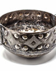 A silver-colored, round metal container with geometric patterns and round handles, crafted from recycled material