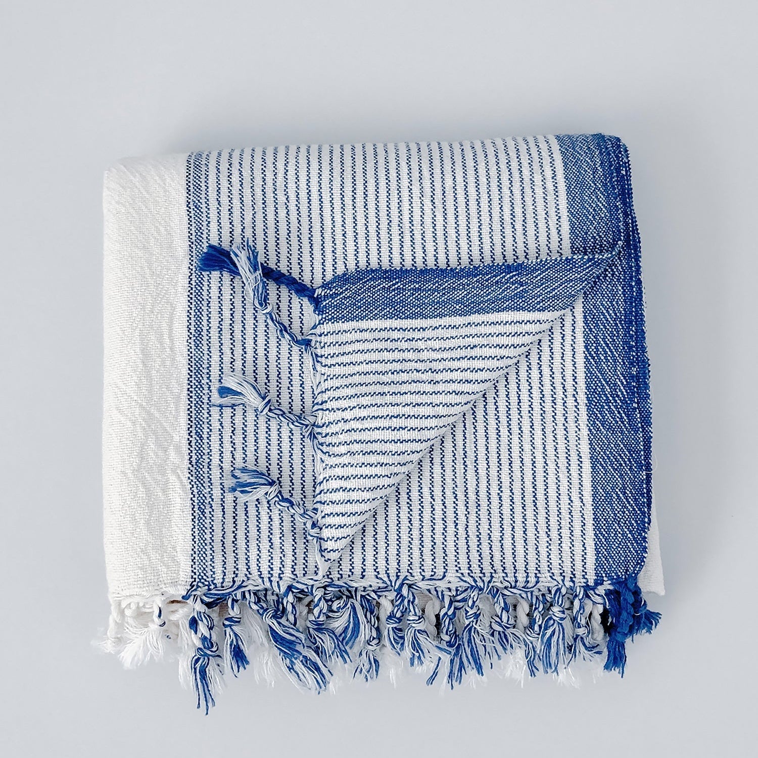 A handwoven ivory and blue striped Turkish towel with fringes displayed on a white background