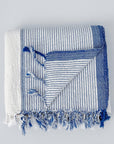 A handwoven ivory and blue striped Turkish towel with fringes displayed on a white background