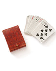 A closed embossed leather box in brown color with intricate floral patterns on the cover alongside the playing cards that go inside of it displayed on a white background.